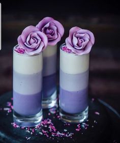 two glasses filled with purple flowers on top of a black plate and sprinkles