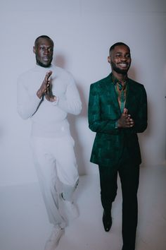 two men standing next to each other in front of a white wall