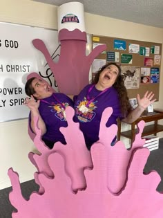 two women standing in front of a large pink object that looks like a giant hand