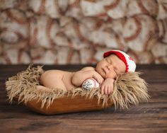 a newborn baby wearing a red and white baseball hat sleeping in a wooden bowl on a wood floor