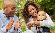 a man and woman holding a baby in their arms while smiling at each other's eyes