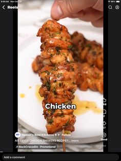 the chicken skewer is being held up by someone's hand on a white plate