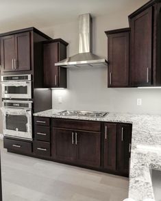 an empty kitchen with granite counter tops and dark wood cabinets, stainless steel range hood over the stove