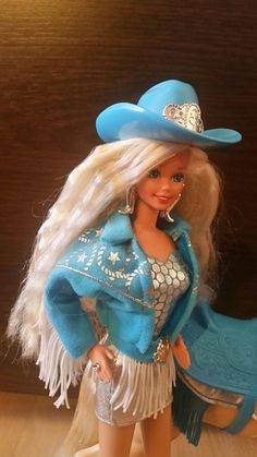 a barbie doll wearing a blue cowboy hat and fringed skirt with a white horse