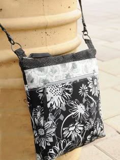 a black and white flowered purse sitting on top of a cement pillar next to a planter