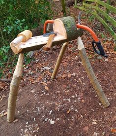 a wooden bench made out of logs and some tools on top of the ground in front of a fence