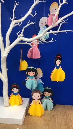 paper dolls are hanging from the branches of a tree in front of a blue wall