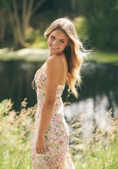 a woman in a floral dress poses for a photo by the water's edge