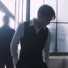 a man standing in front of a window wearing a black vest