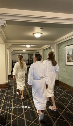 three women in white robes walking down a hallway