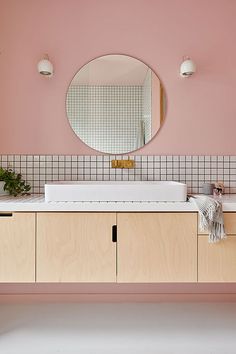 a bathroom with pink walls and white counter tops, along with a round mirror above the sink