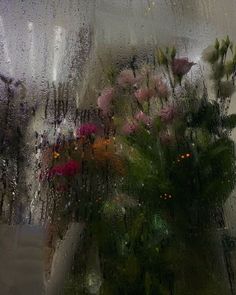 a vase filled with lots of flowers sitting on top of a window covered in rain