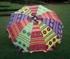 an open colorful umbrella sitting on top of a lush green grass covered field next to trees