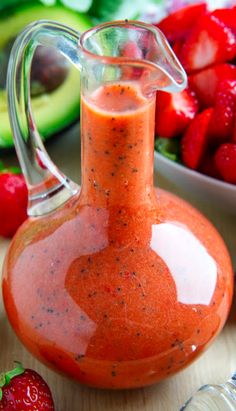 a glass pitcher filled with dressing next to sliced strawberries and avocado in the background