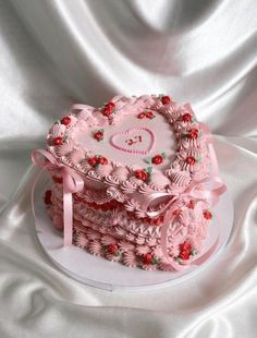 a heart shaped cake with pink frosting and red berries on top, sitting on a white cloth