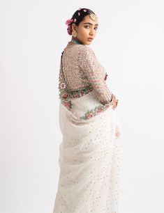 a woman wearing a white sari with pink flowers in her hair, standing and looking off to the side