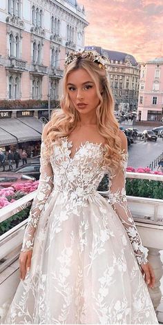 a woman standing on top of a balcony wearing a white wedding dress with long sleeves