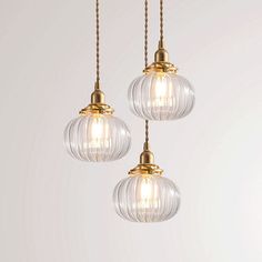 three clear glass globe pendant lights hanging from a gold colored corded chandelier