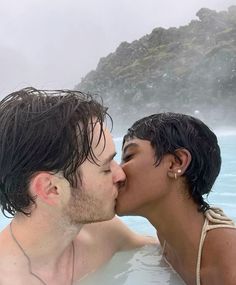 two people in a hot tub kissing each other with steam coming out of the water behind them