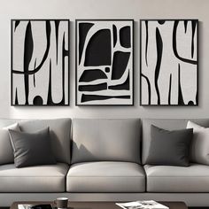 two black and white paintings on the wall above a couch in a living room with gray pillows