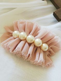 three pearls are attached to a pink fabric hair clip on a white cloth bed sheet