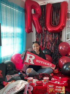 a woman sitting on the floor holding up a sign that says rutgers with balloons surrounding her