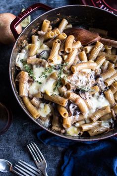 a skillet filled with pasta and mushrooms on top of a blue cloth next to an onion