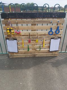 a wooden pallet with clipboards and scissors attached to it, hanging on a fence