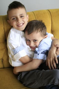 two young boys hugging each other while sitting on a yellow couch with their arms around each other