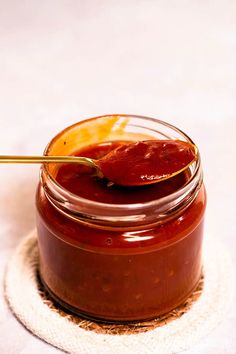 a spoon in a jar filled with sauce on top of a white cloth covered table