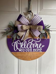 a welcome sign hanging on the front door with purple and gold ribbon around it that says, welcome to our home