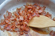 bacon is being cooked in a pan with a wooden spoon