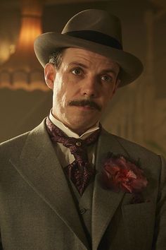 a man wearing a suit and tie with a flower in his lapel, looking at the camera