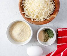 two bowls filled with different types of cheese next to an egg and other ingredients on a white surface