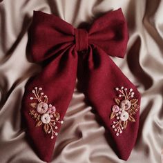 a red bow with flowers on it laying on a white satin bed sheet next to a teddy bear