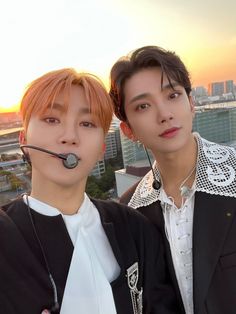 two young men with headsets on in front of a cityscape at sunset