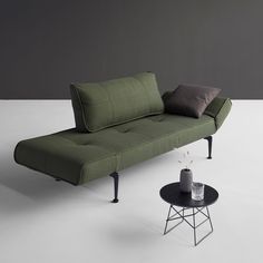 a green couch sitting on top of a white floor next to a table with a vase