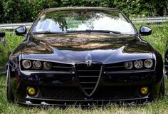 the front end of a black sports car parked on grass next to trees and bushes