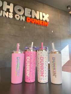 four different colored cups sitting on top of a table next to a neon sign that reads phoenix turns on dunkin