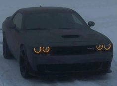 the front end of a black sports car in the snow with its lights turned on