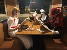 two women dressed in costumes sitting at a table with books and magazines on it,