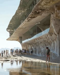 many people are standing near the water and under an overhanging structure that looks like a cliff