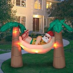 an inflatable santa clause laying on a hammock with palm trees and lights