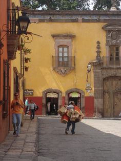 people walking down the street in front of an old yellow building with red and white trim