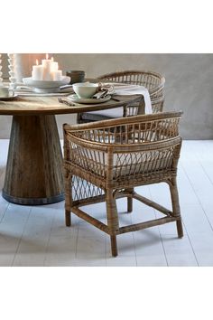 the table is set with candles and plates on it, along with two wicker chairs