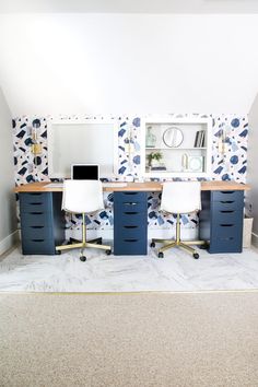 two desks with blue drawers and white chairs in front of a wallpapered room