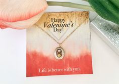 a valentine's day card with a heart pendant on it next to a flower