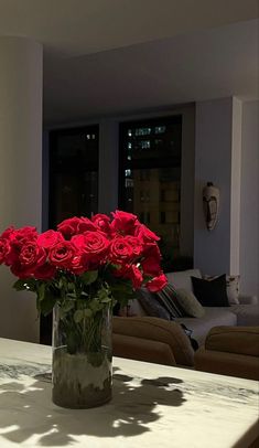 a vase filled with red roses sitting on top of a table next to a couch