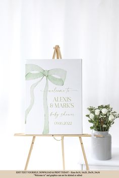 a white canvas with a green bow on it sitting next to a potted plant