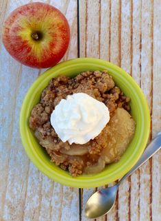 an apple crisp with whipped cream in a green bowl next to an apple on a wooden table